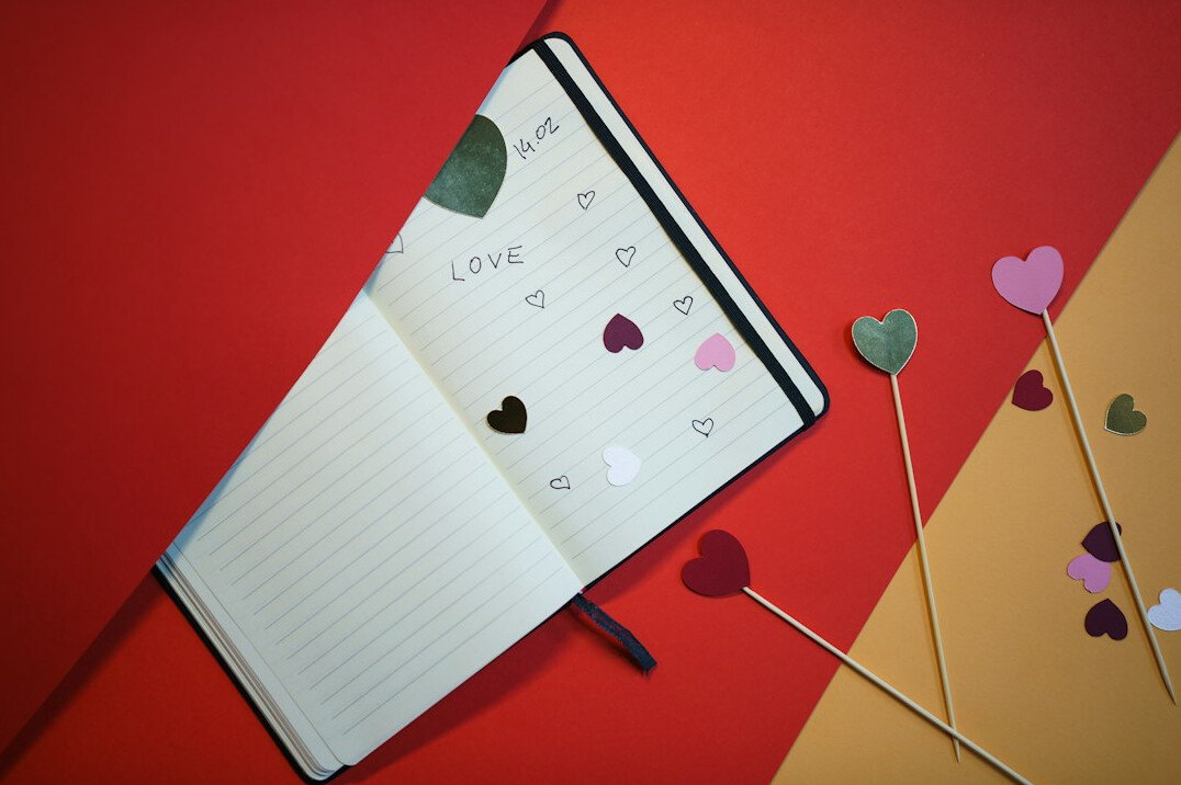 Hand writing notes in a notebook next to a laptop